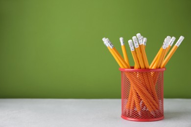 Many sharp pencils in holder on light table against green background, space for text