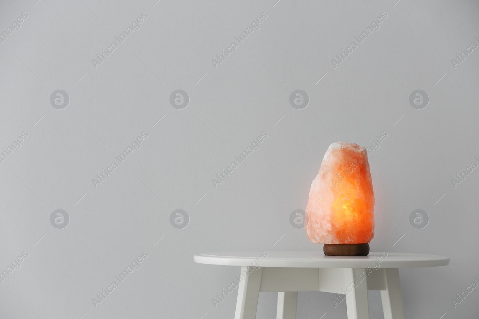 Photo of Himalayan salt lamp on table against white background. Space for text