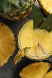 Tasty pineapple smoothie and fruit on grey table, flat lay