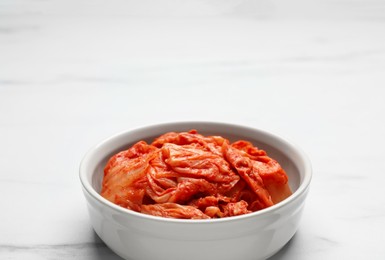 Bowl of spicy cabbage kimchi on white marble table. Space for text