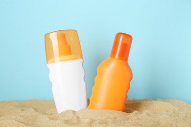 Photo of Suntan products on sand against light blue background