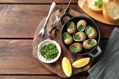 Photo of Delicious cooked snails in baking dish served on wooden table, flat lay
