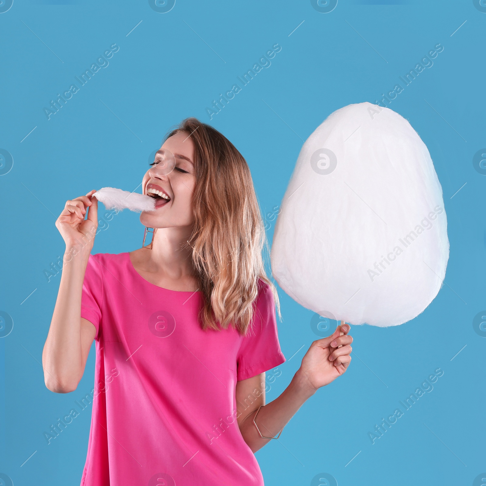 Photo of Happy young woman eating cotton candy on blue background