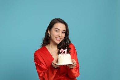 Photo of Coming of age party - 21st birthday. Woman holding cake with number shaped candles on light blue background