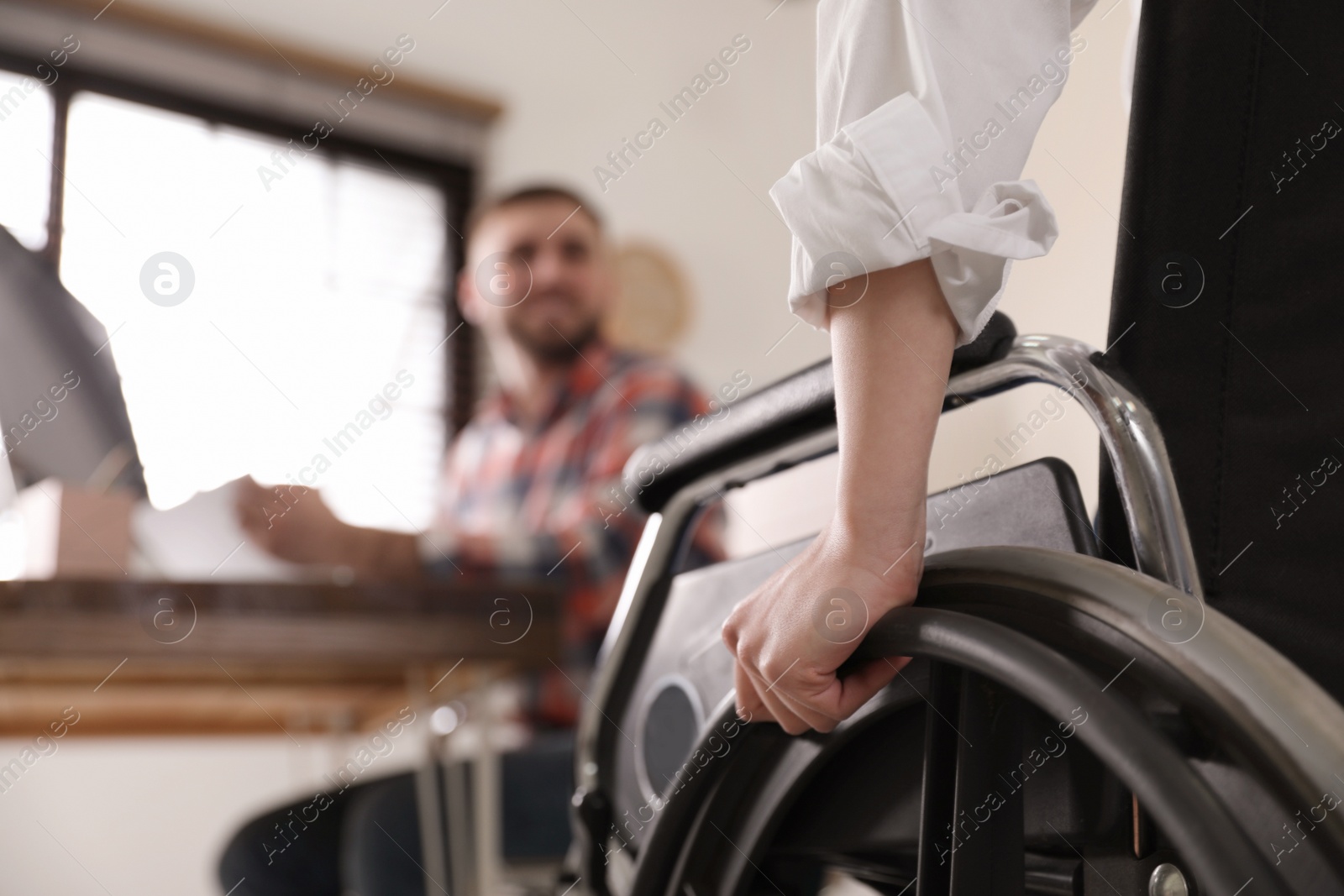 Photo of Woman in wheelchair with her colleague at workplace, closeup