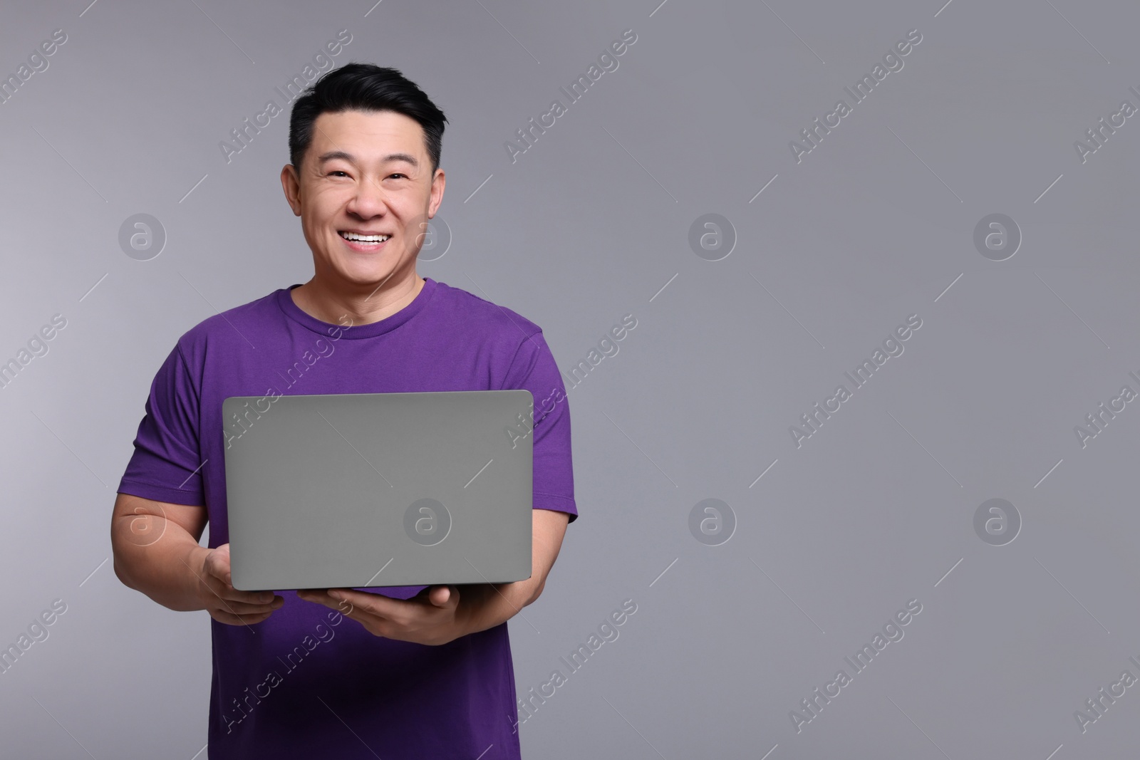 Photo of Happy man with laptop on grey background, space for text