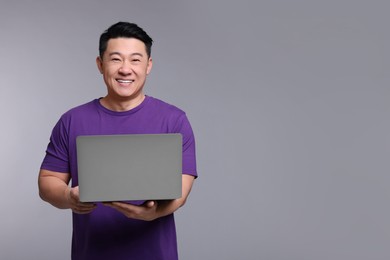 Photo of Happy man with laptop on grey background, space for text