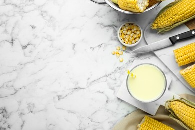 Photo of Tasty fresh corn milk in glass and cobs on marble table, flat lay. Space for text