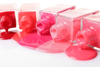 Photo of Spilled different nail polishes with bottles on white background, closeup