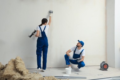 Photo of Professional workers plastering wall with putty knives indoors