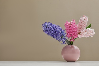 Beautiful hyacinths in vase on table against color background, space for text. Spring flowers