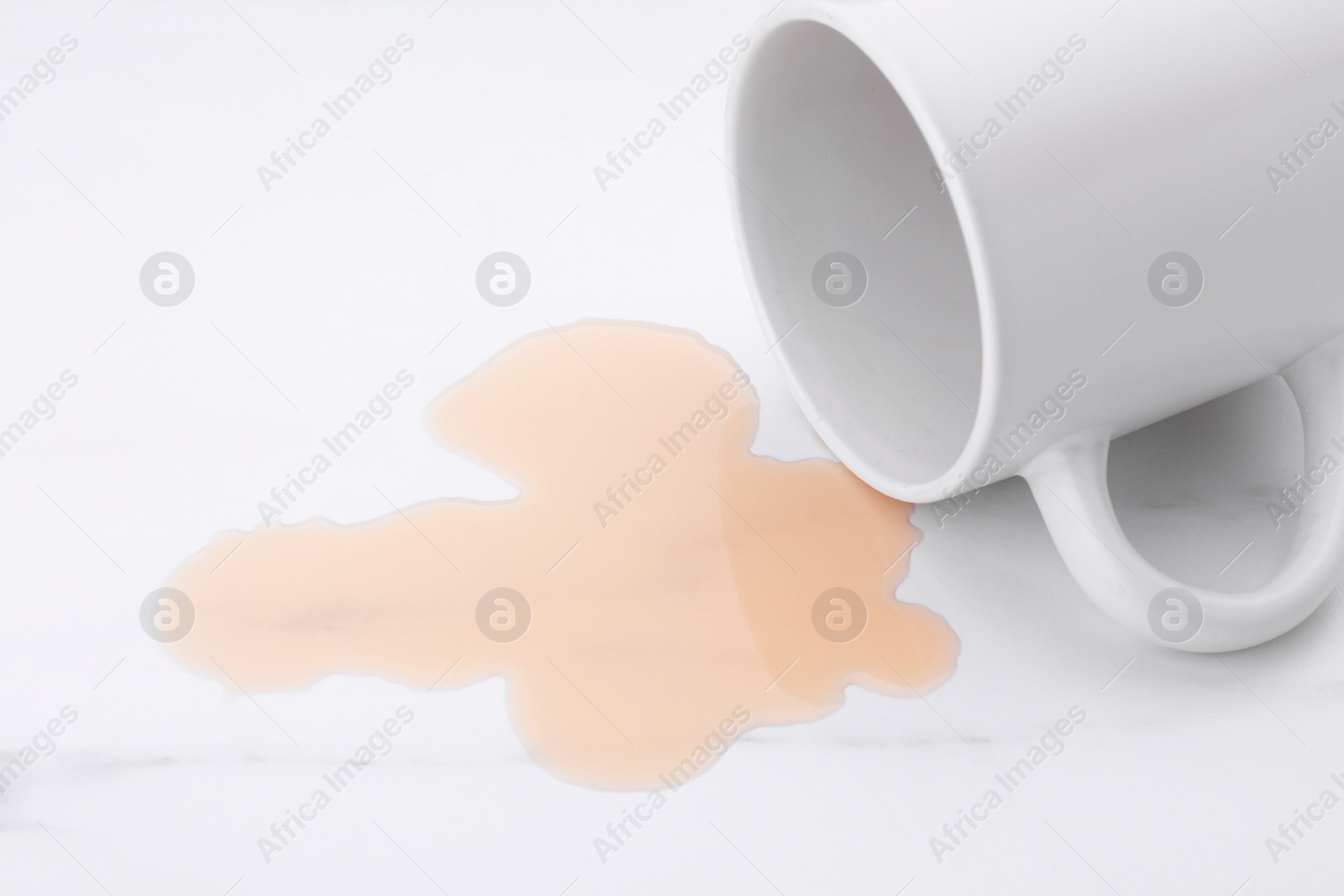 Photo of Puddle of liquid and overturned mug on white marble table, closeup
