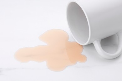 Puddle of liquid and overturned mug on white marble table, closeup