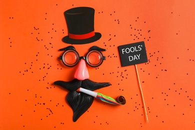 Photo of Funny face made with clown's accessories on red background, flat lay