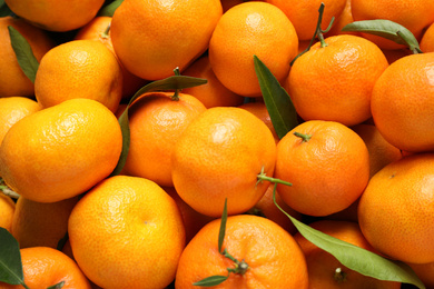 Photo of Fresh ripe tangerines with leaves as background, top view. Citrus fruit