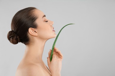 Young woman with aloe vera leaf on light grey background. Space for text