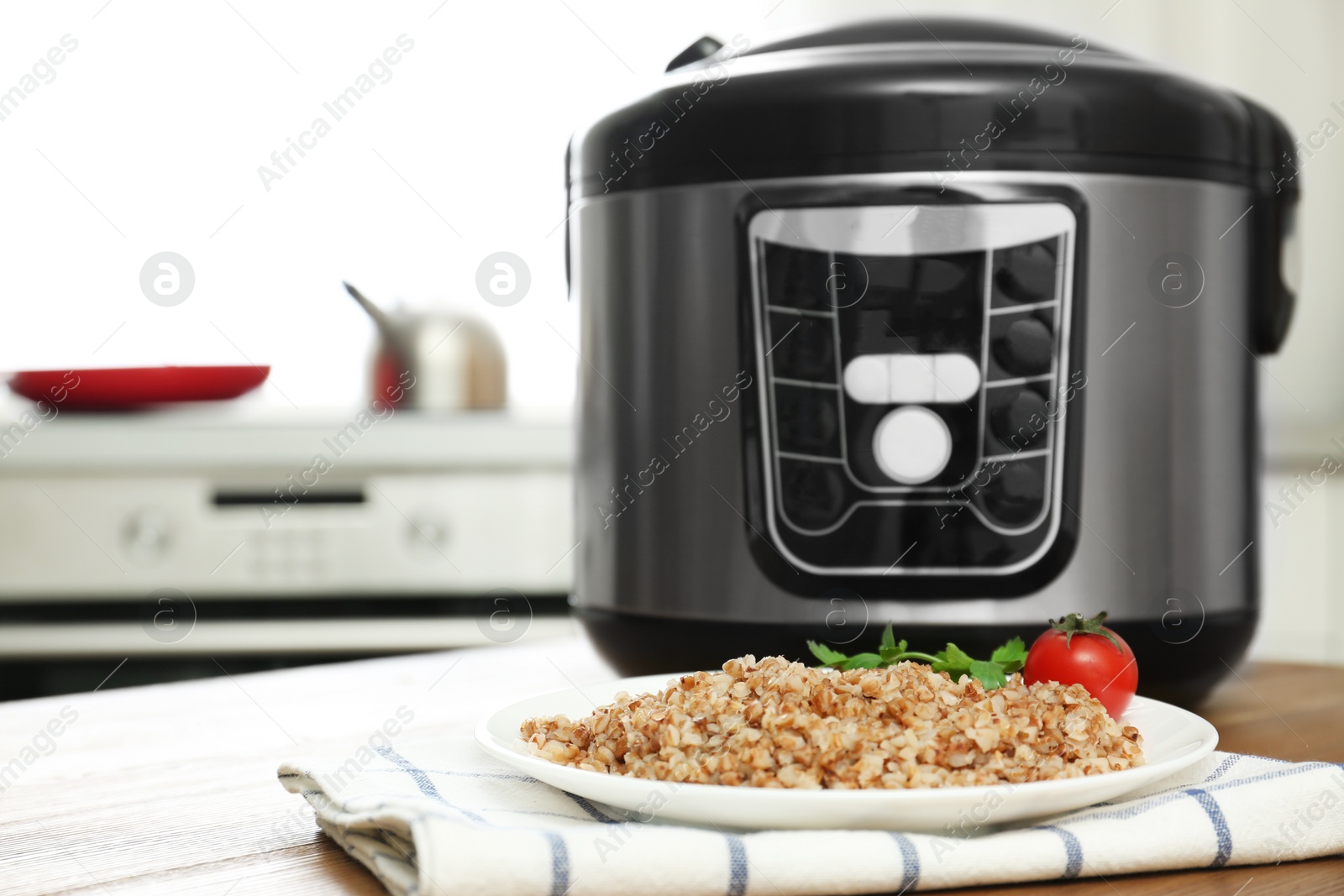 Photo of Plate with delicious buckwheat and multi cooker on table in kitchen. Space for text