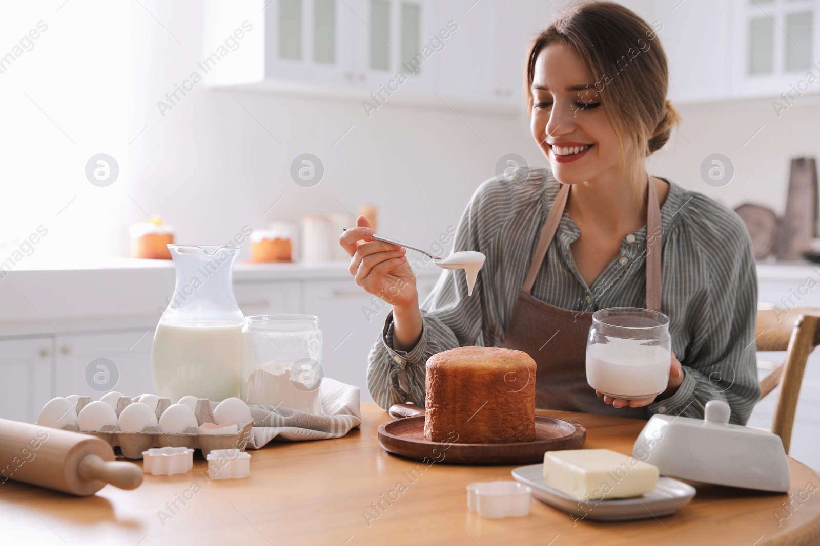 Photo of Young woman decorating traditional Easter cake with glaze in kitchen