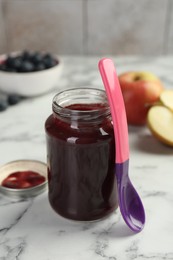 Photo of Tasty baby food in jar and spoon on white marble table