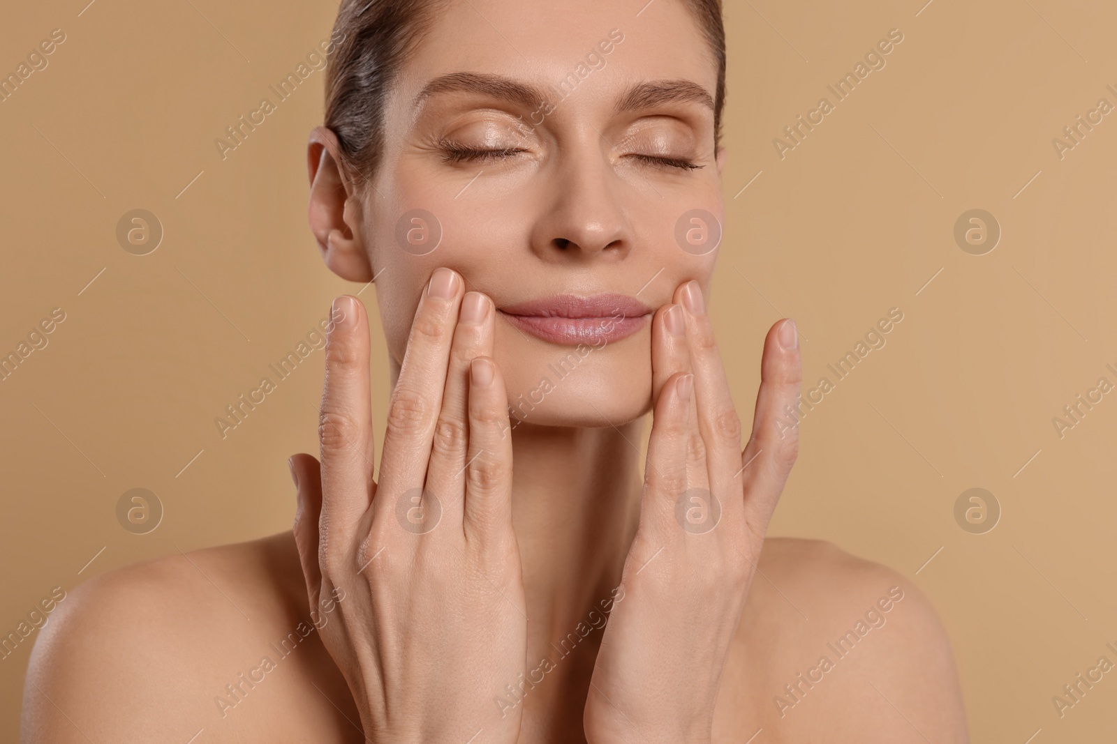 Photo of Woman massaging her face on beige background