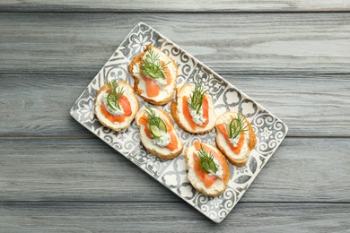 Photo of Tasty canapes with salmon, cucumber, cream cheese and dill on wooden table, top view