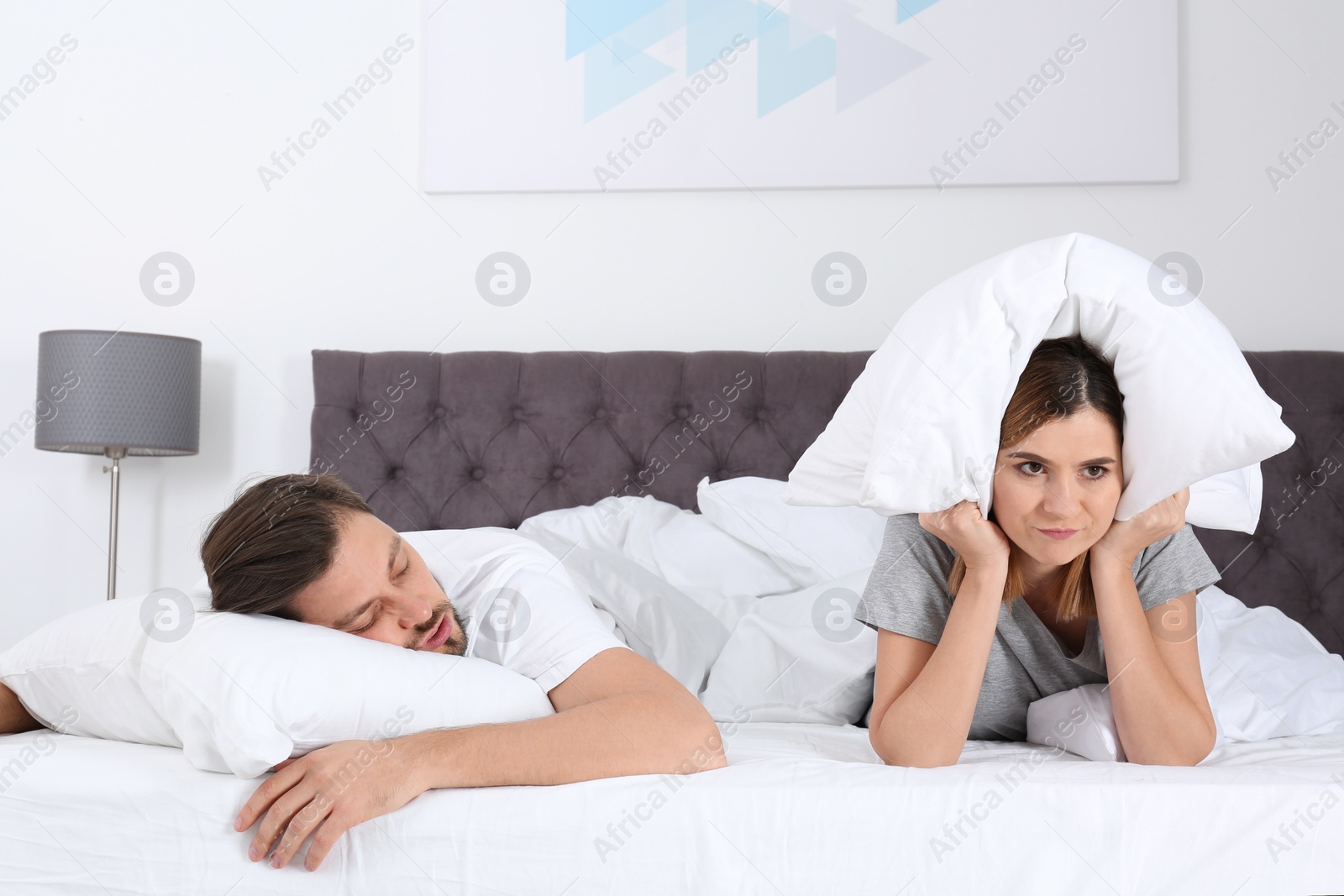 Photo of Upset woman covering her head with pillow near sleeping husband in bedroom. Relationship problems