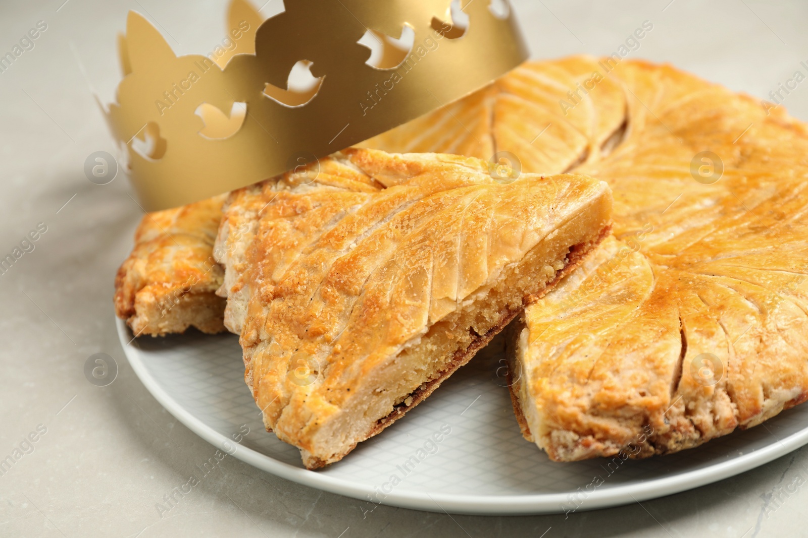 Photo of Traditional galette des Rois with paper crown on light grey marble table