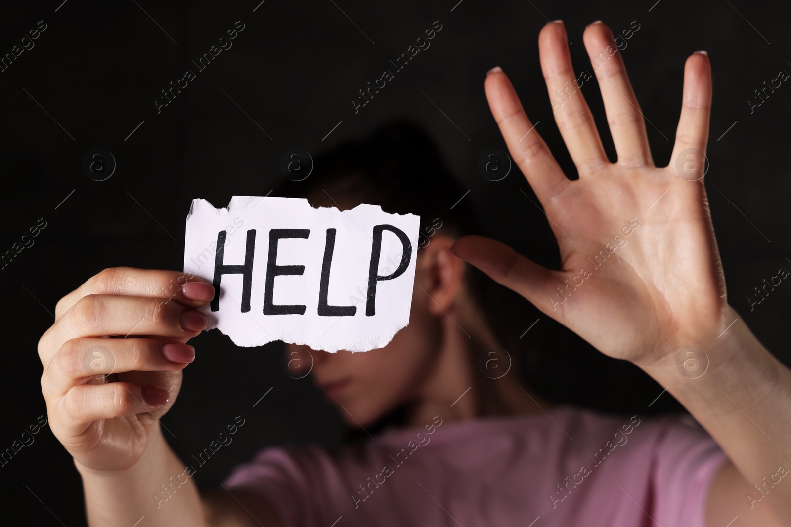 Photo of Woman holding piece of paper with word Help on dark background, closeup. Domestic violence concept