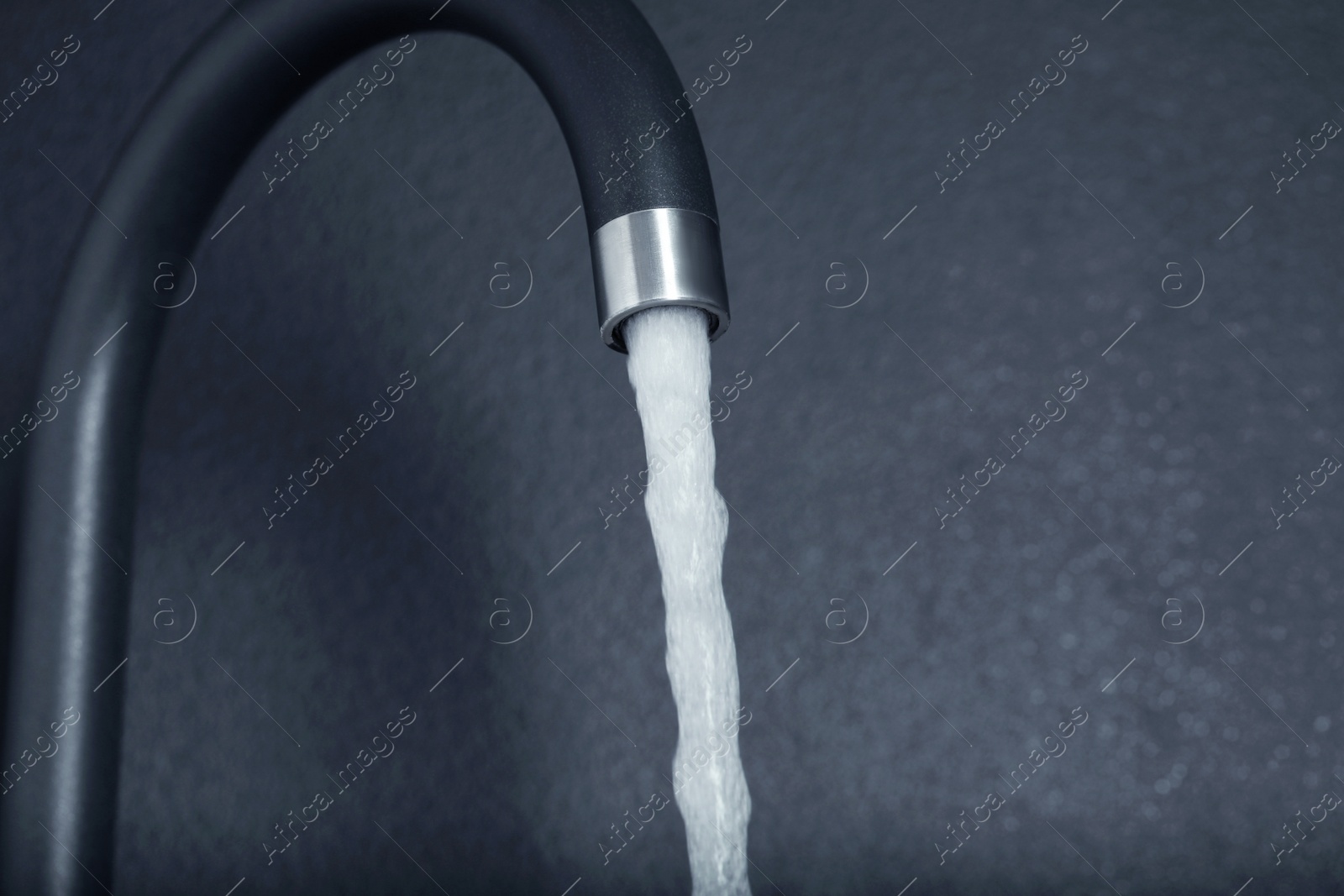 Photo of Stream of water flowing from tap on dark background, closeup. Space for text