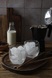 Making iced coffee. Ice cubes in glasses and straws on wooden table