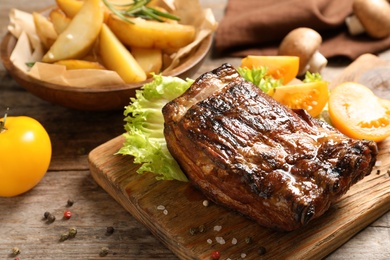 Photo of Delicious barbecued ribs served with garnish on wooden board