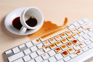 Cup of coffee spilled over computer keyboard on wooden table