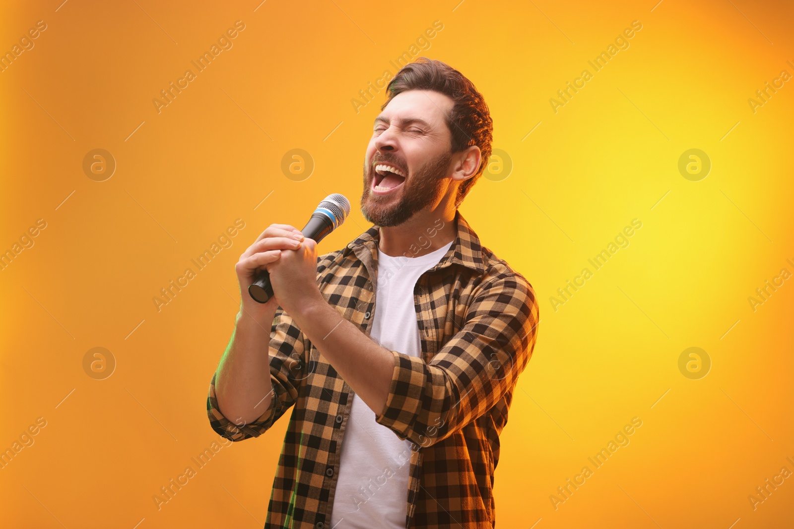 Photo of Handsome man with microphone singing on golden background