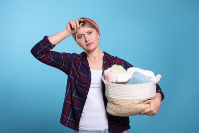 Photo of Tired woman with basket full of laundry on light blue background