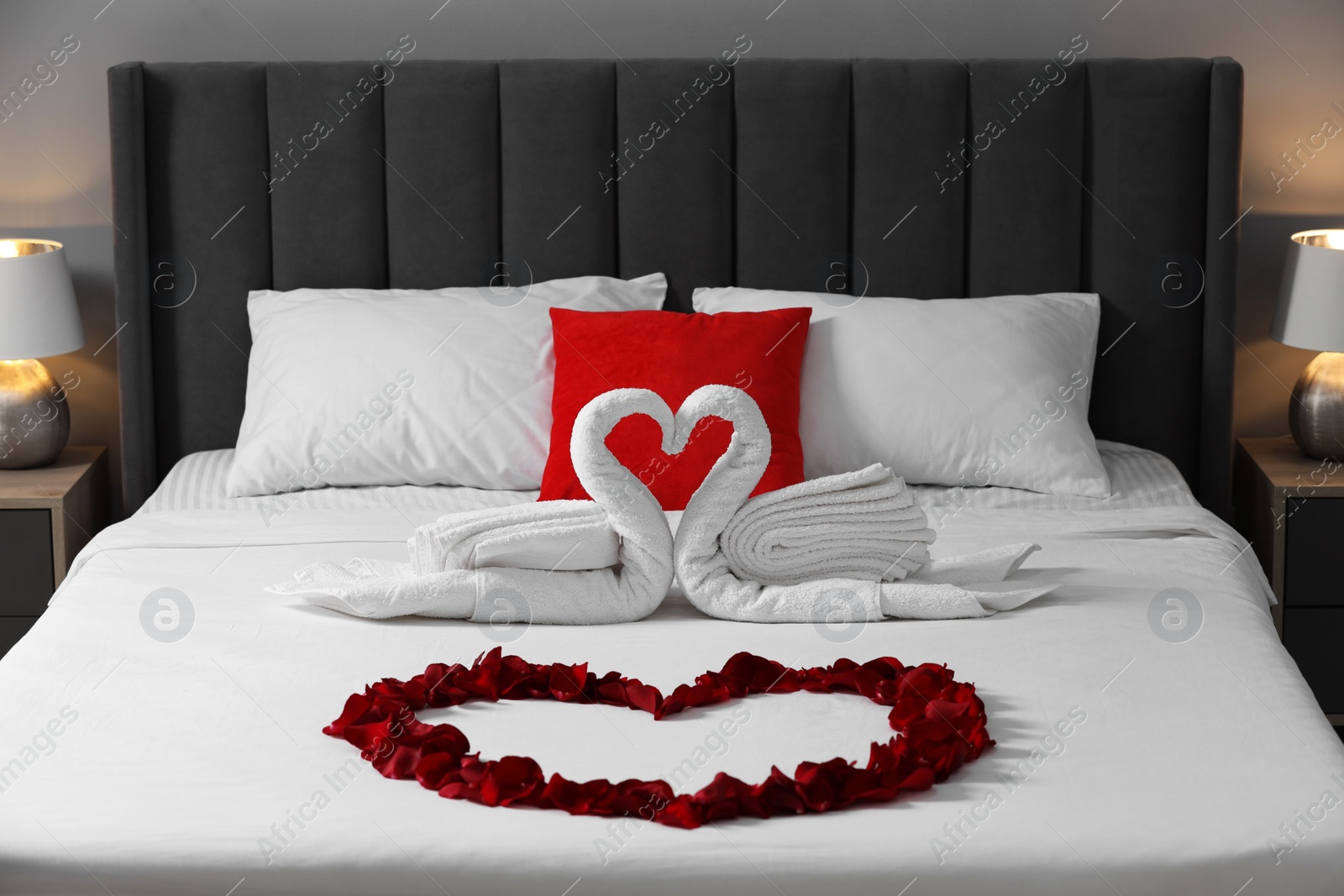 Photo of Honeymoon. Swans made with towels and heart of beautiful rose petals on bed in room