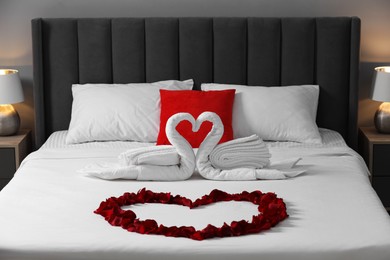 Honeymoon. Swans made with towels and heart of beautiful rose petals on bed in room