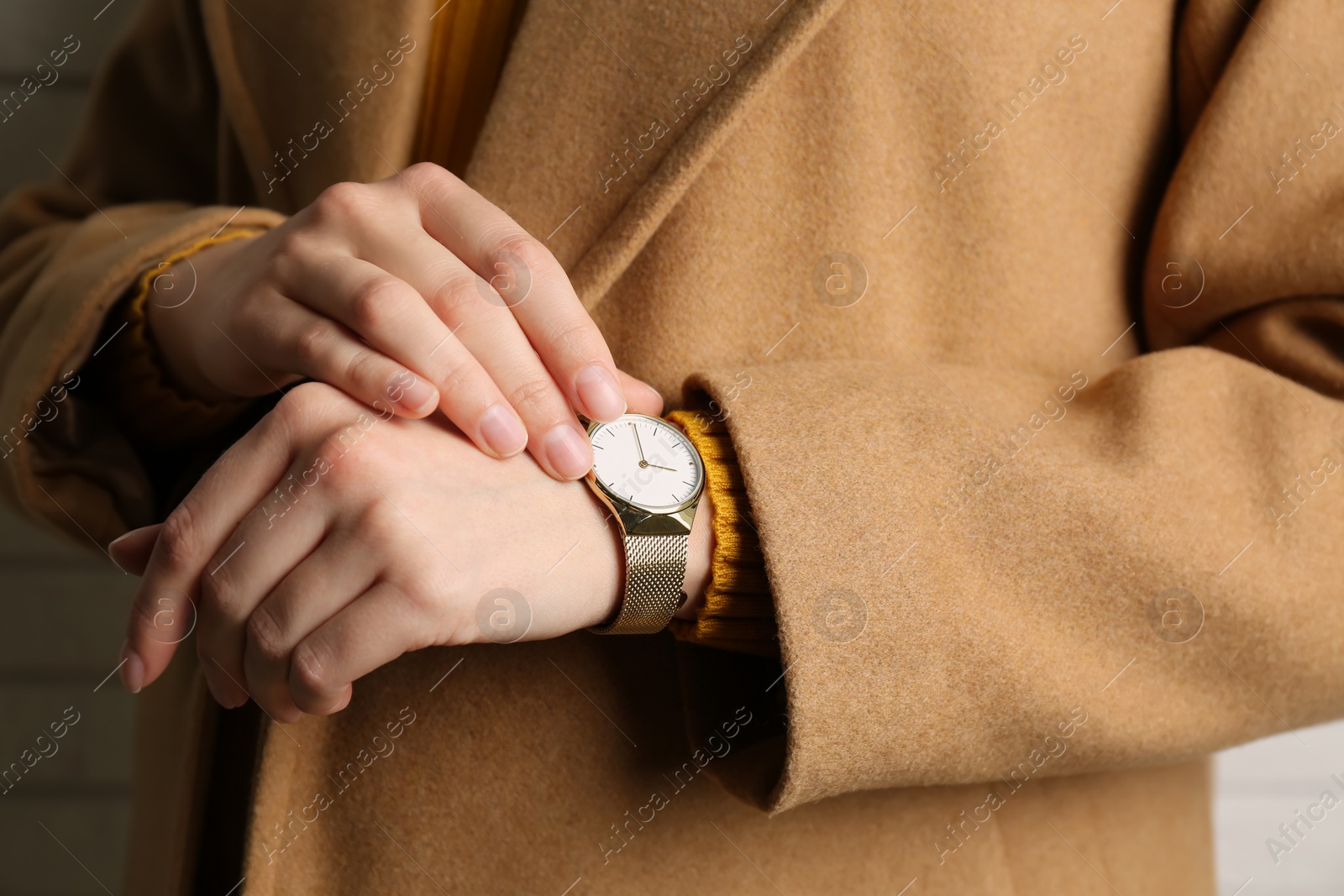 Photo of Woman wearing luxury wristwatch near white brick wall, closeup