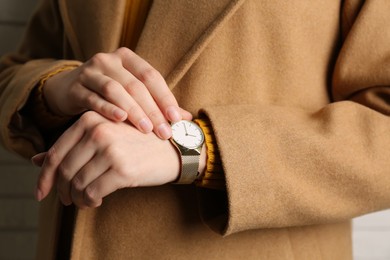 Photo of Woman wearing luxury wristwatch near white brick wall, closeup