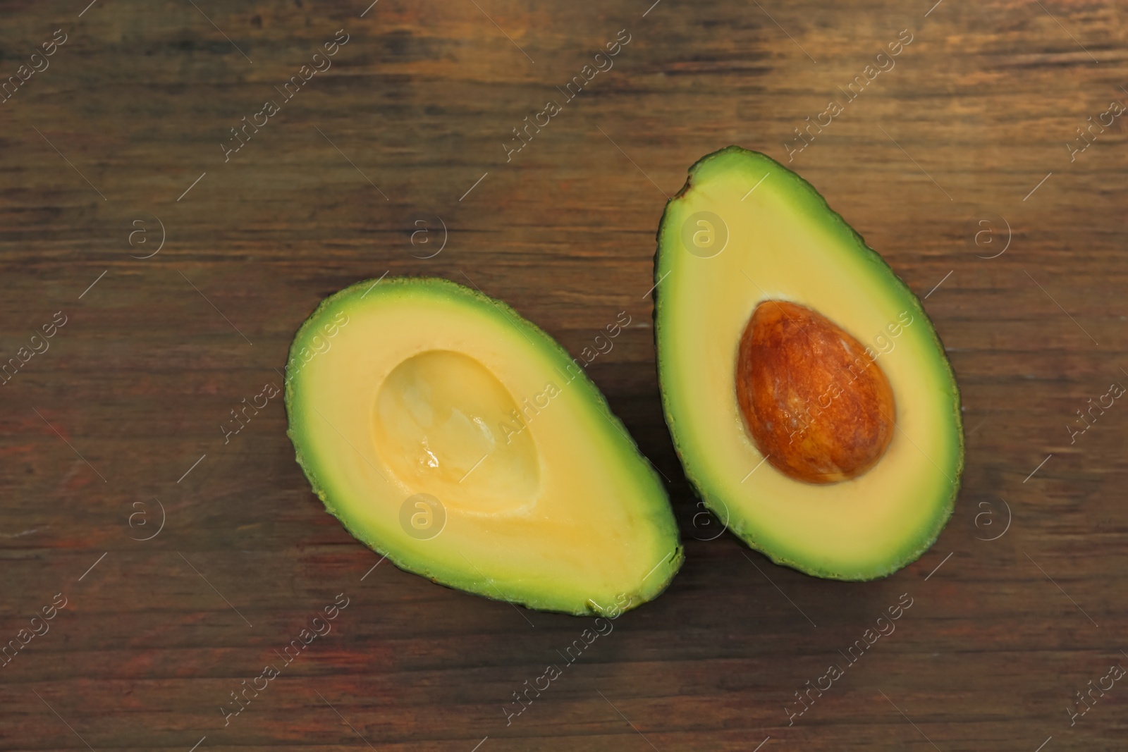 Photo of Halves of fresh avocado on wooden table, flat lay