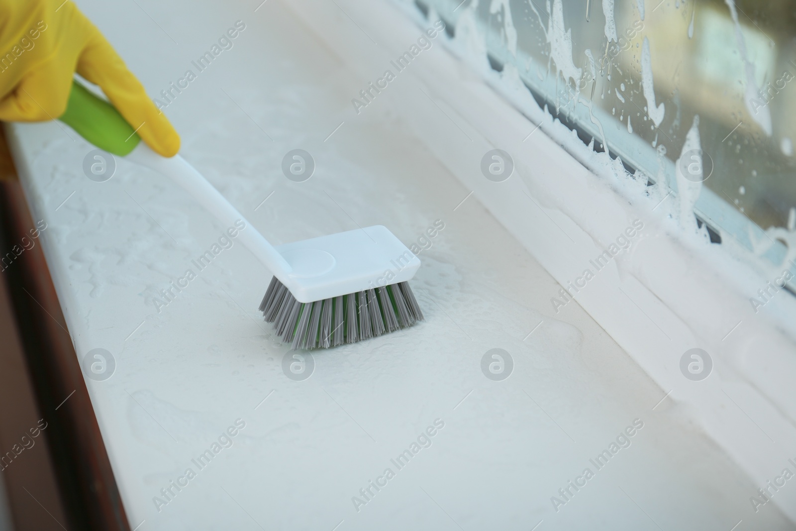 Photo of Woman cleaning window sill with brush, closeup