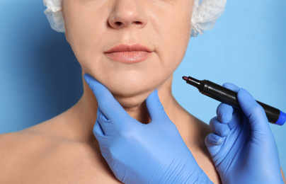 Photo of Surgeon with marker preparing woman for operation against blue background, closeup. Double chin removal