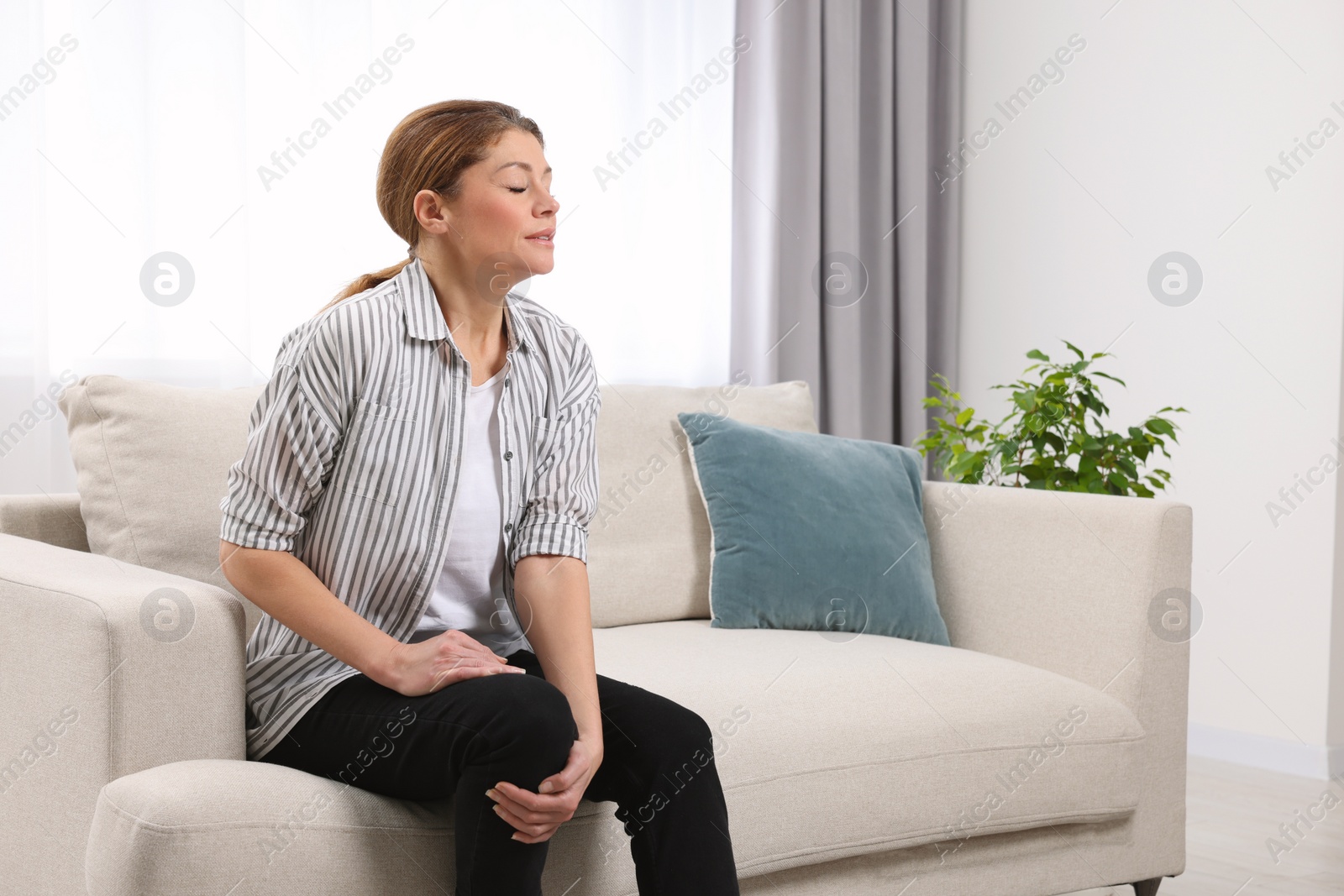 Photo of Woman suffering from knee pain on sofa indoors. Arthritis symptoms