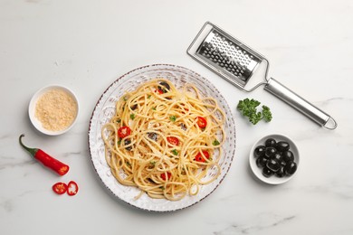 Photo of Plate of delicious pasta with olives, tomatoes and parmesan cheese near ingredients on white marble table, flat lay