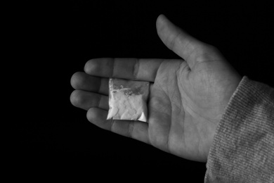 Photo of Drug dealer holding bag with cocaine on black background, closeup