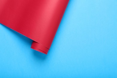 Roll of red wrapping paper on light blue background, top view. Space for text
