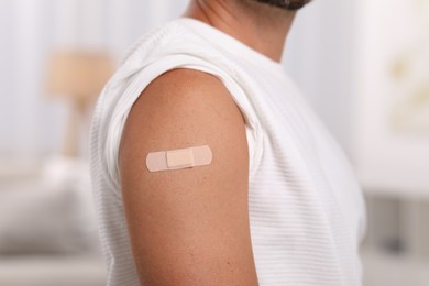 Photo of Man with sticking plaster on arm after vaccination at home, closeup