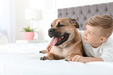 Cute little child with his dog resting on bed at home