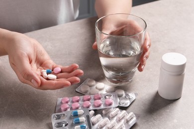 Photo of Woman with different pills and glass of water at grey table, closeup