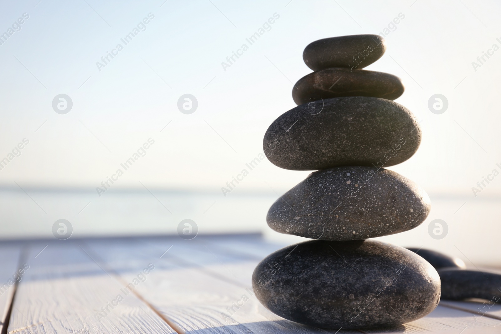 Photo of Stack of dark stones on wooden deck near sea. Zen concept