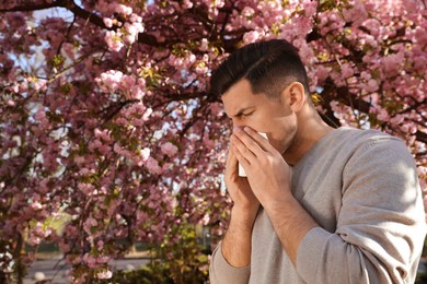 Man suffering from seasonal pollen allergy near blossoming tree outdoors